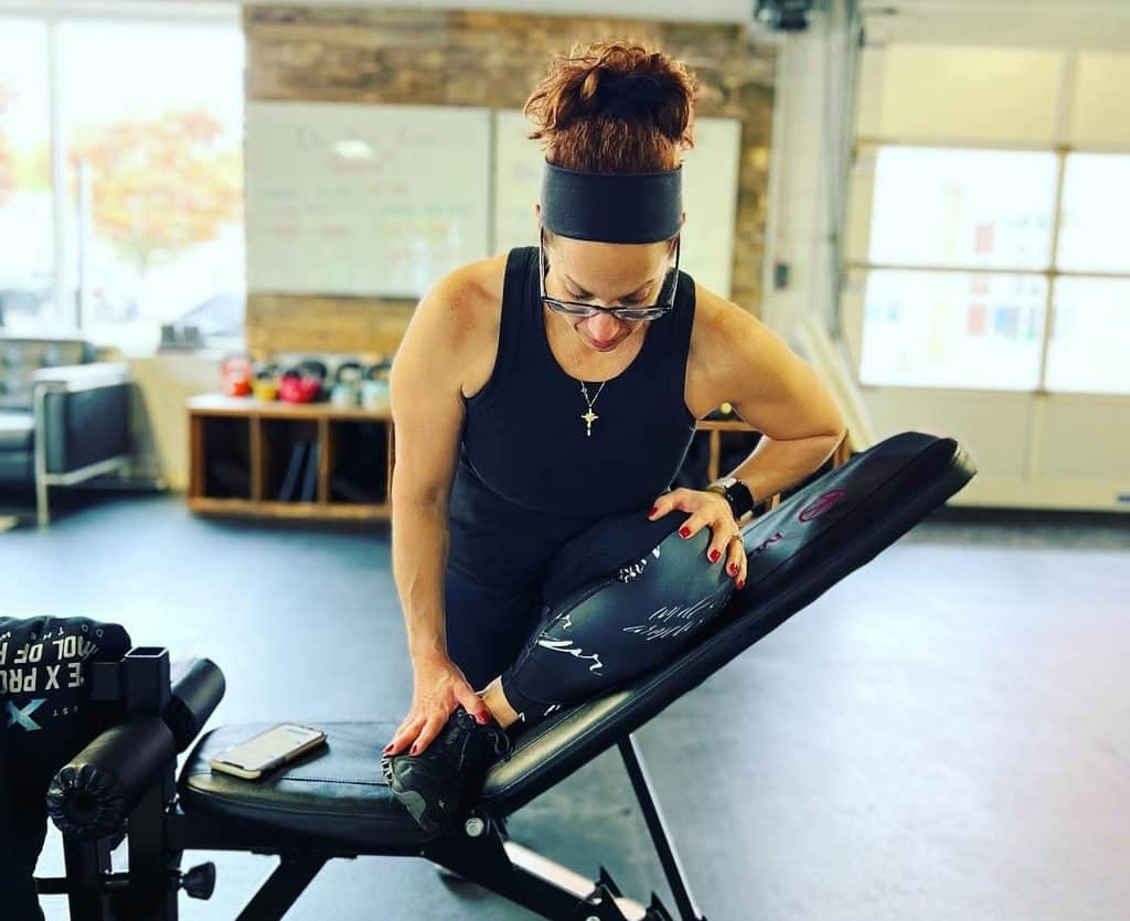 A breast cancer survivor in workout clothes stretches her leg on an inclined gym bench.
