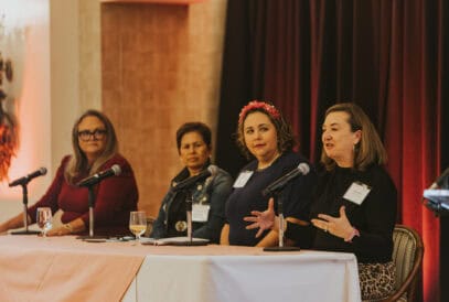 Four women sit at a table at the Susan G. Komen EmpowerED: Education After Diagnosis event. The woman on the far right is speaking and the three other women are watching.