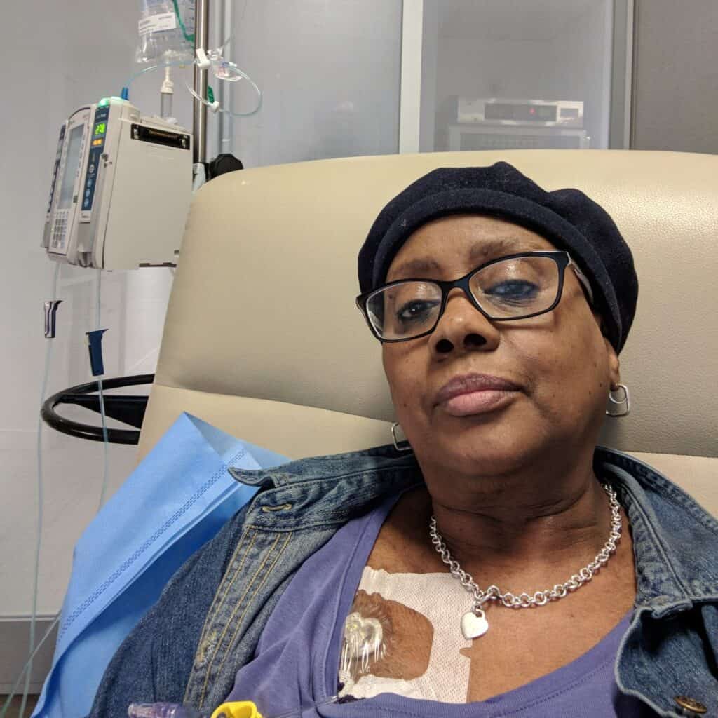 Frances receives breast cancer treatment. She's sitting in a chair in a hospital room.