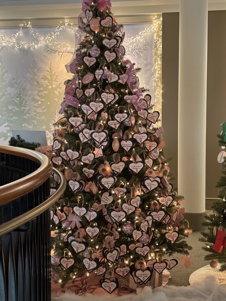 A Christmas tree stands in a lobby, covered with pink ribbon and featuring hundreds of handmade ornaments that honor breast cancer survivors.