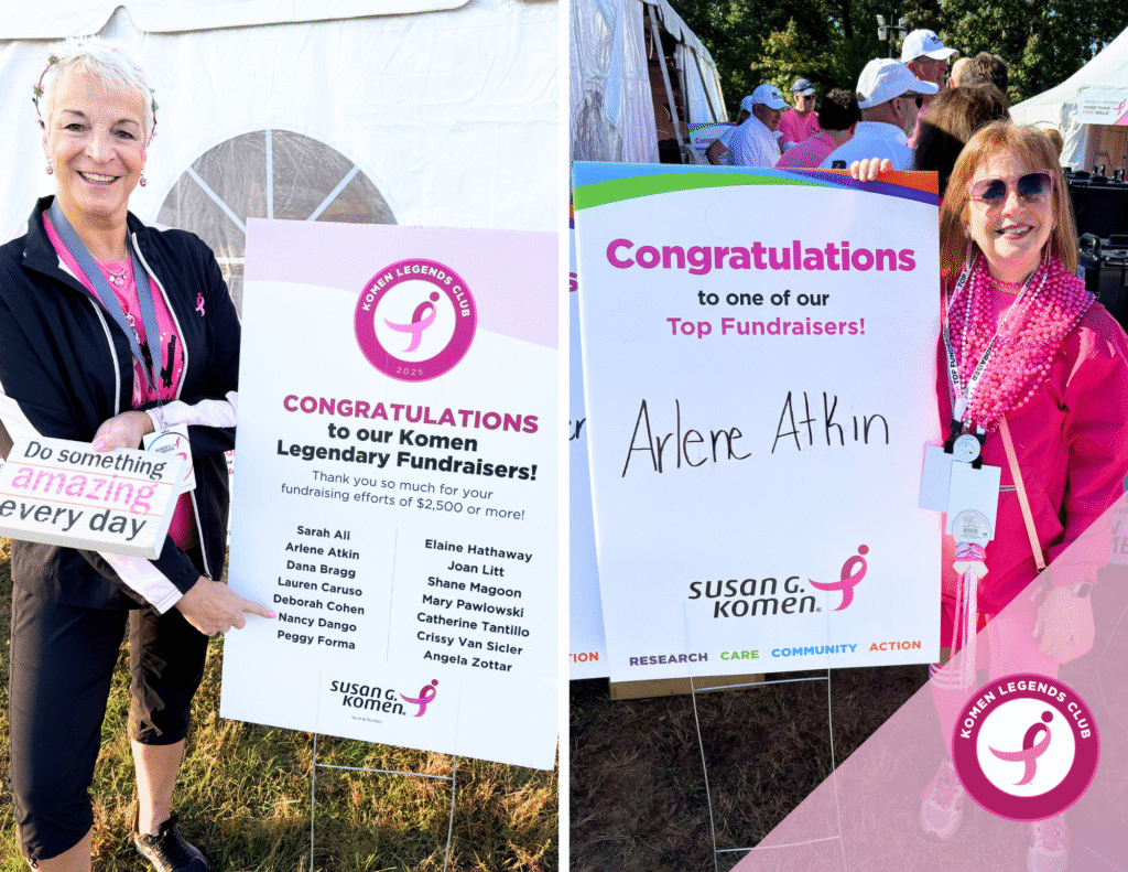 Two women at an outdoor event celebrate as members of the Komen Fundraising Legends Club. One holds a sign listing honorees, pointing at her name on the board, while Arlene Atkin poses proudly by her own sign. Both sport pink outfits and bright smiles.
