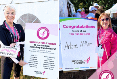Two women at an outdoor event celebrate as members of the Komen Fundraising Legends Club. One holds a sign listing honorees, pointing at her name on the board, while Arlene Atkin poses proudly by her own sign. Both sport pink outfits and bright smiles.