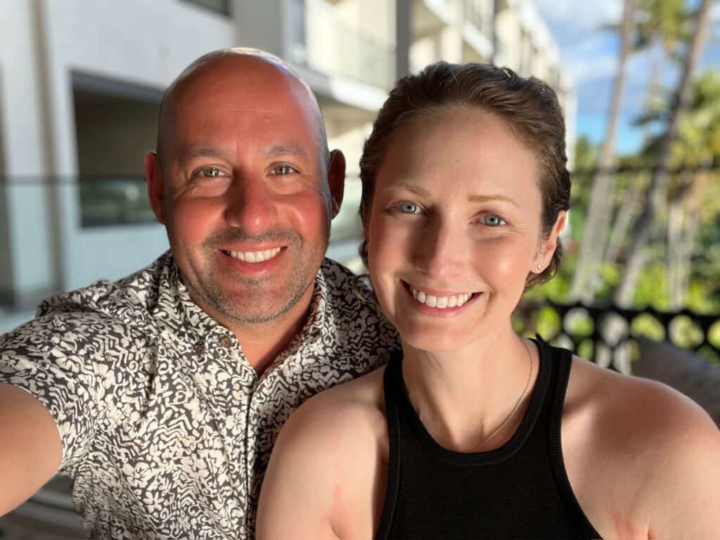 Lauren and her husband are sitting outside. Her hair is short. They are smiling.