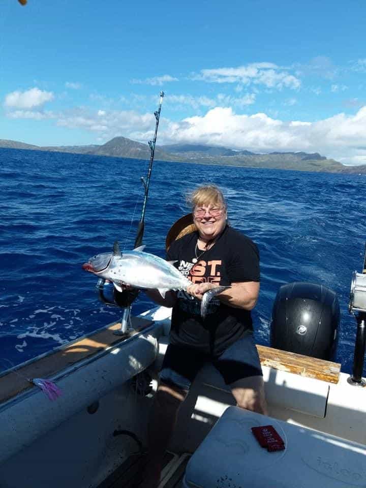 Person sitting on a boat holding a large fish with the ocean and distant mountains in the background under a partly cloudy sky.