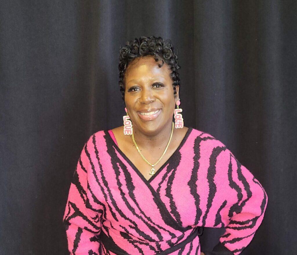 Tennille, living with metastatic breast cancer, smiles at the camera, wearing pink and black.