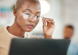 A black woman wearing glasses studies her computer screen.
