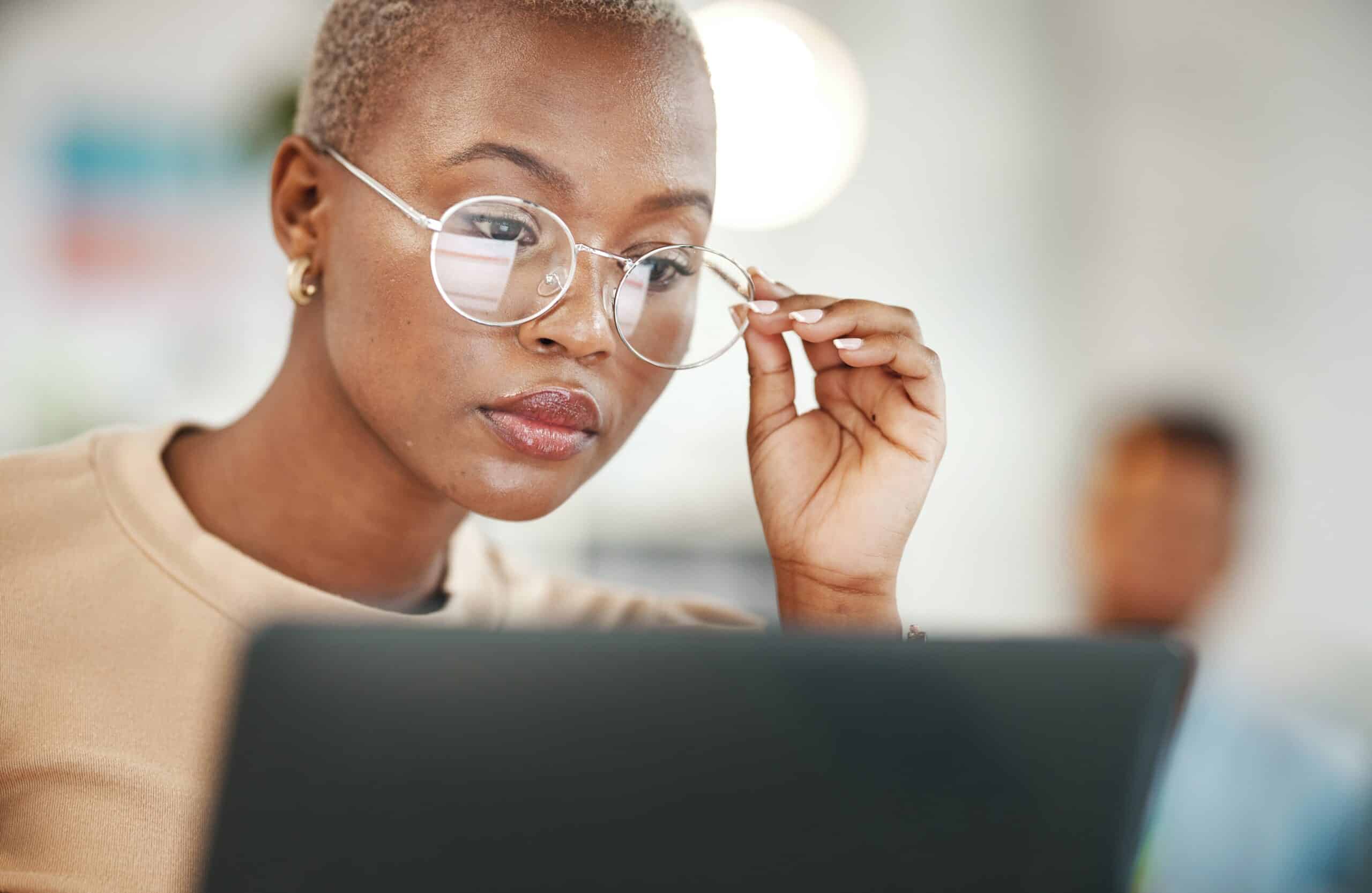 A black woman wearing glasses studies her computer screen.