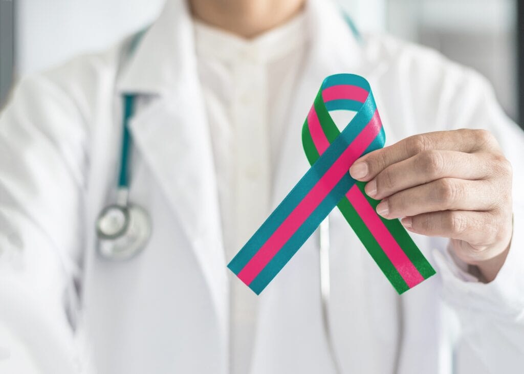 A doctor holds a metastatic breast cancer ribbon, which is teal, green and pink.
